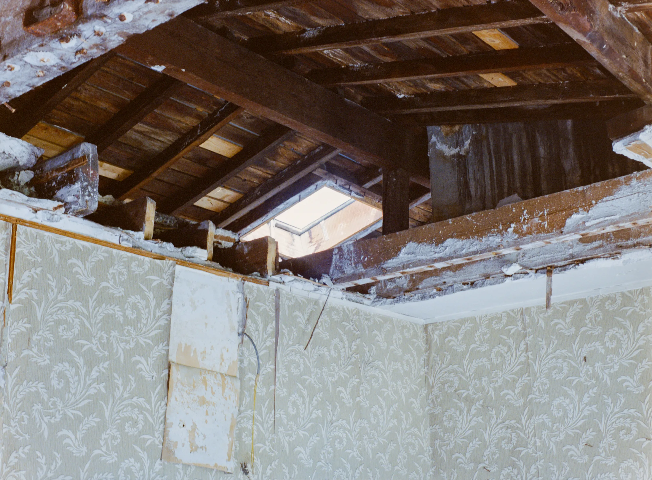 Roof opening above a wall with remnants of patterned wallpaper
